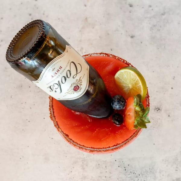 A Cook's Brut champagne bottle inverted into a red margarita with lime, blueberries, and strawberry.
