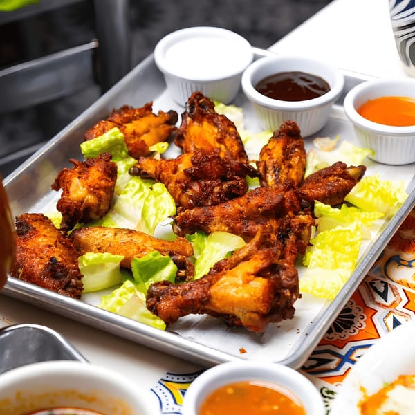 El Paso Tacos & Tequila's crispy chicken wings with lettuce and three dipping sauces on a metal tray.