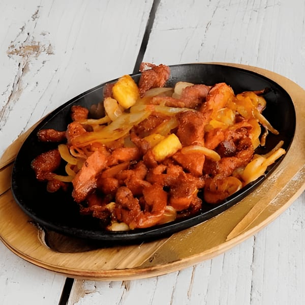Sizzling Mexican fajitas with chicken, onions, and bell peppers in a black skillet on a wooden board.
