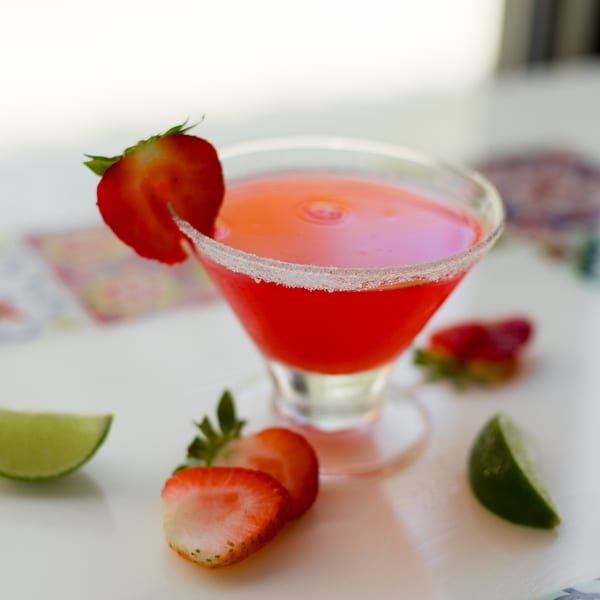 A vibrant strawberry margarita in a salt-rimmed glass, garnished with fresh strawberries and lime.