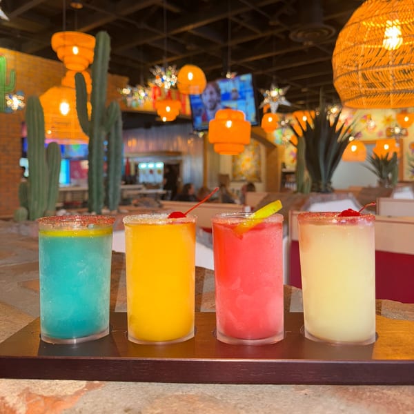 Four colorful frozen margaritas on a tray in a vibrant El Paso Tacos & Tequila restaurant setting.