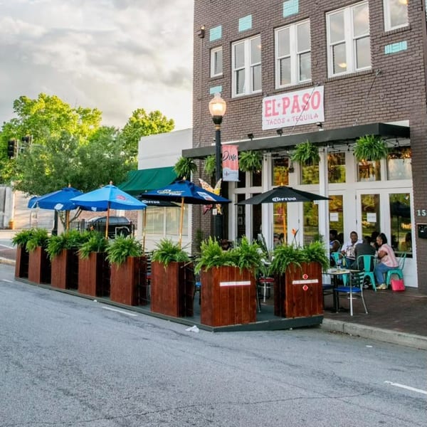 El Paso Tacos + Tequila restaurant exterior with outdoor seating, blue and black umbrellas, and patrons.