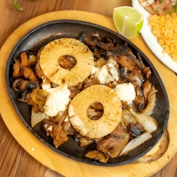 Sizzling Mexican fajitas with grilled pineapple, onions, and meat, served with a lime wedge.